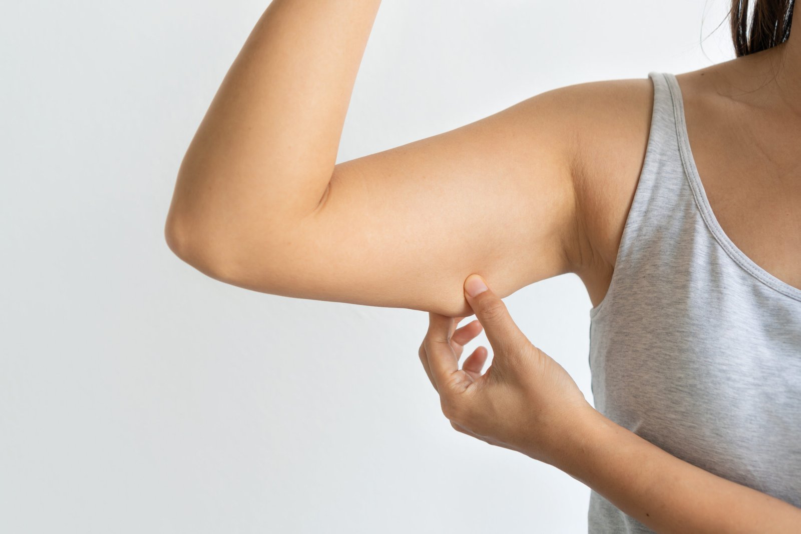 Closeup of young Asian woman pinching arm fat flabby skin, Female pulling excess fat. Hand and body care concept.
